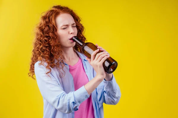 Encaracolado ruiva mulher gengibre beber cerveja e sentir mau humor em csudio fundo amarelo — Fotografia de Stock