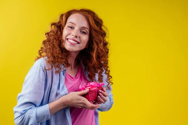 Förvånad rödhårig ingefära lockigt kvinna som håller presenter lådor och känsla chock känslor i studio gul bakgrund — Stockfoto