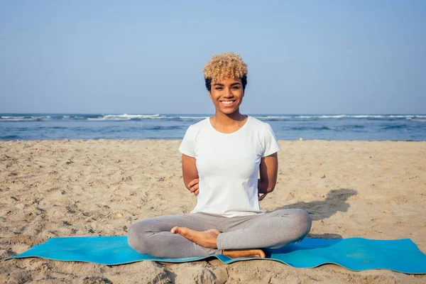 Portrait of a young latin african woman sitting in yoga pose at the beach lifestyle — Stock Photo, Image