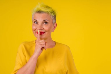 Sıcak elbiseli, renkli sarı boyalı saçları olan ve dudaklarında kırmızı ruj olan pozitif, olgun bir kadın. Jest stüdyosu fotokopisi. Yaşlanma karşıtı yüz jimnastiği.