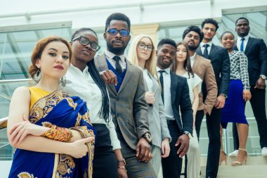 Ofiste çalışan bir grup başarılı Afro-Amerikalı, Avrupalı, Arap ve Koreli ve Hintli işadamı ve işkadını büyük cam pencereli