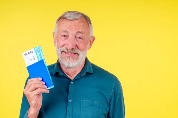 Homme âgé souriant tenant un passeport en couverture bleue et billets studio fond jaune — Photo