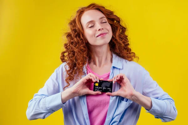 Attraktiv rödhårig lockigt ingefära kaukasiska affärskvinna bär bomull skjorta, innehar kreditkort studio gul bakgrund svart fredag försäljning — Stockfoto