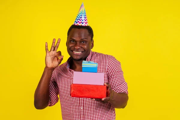 Счастливый африканский американец держит коробки с подарками на день рождения в студии желтый фон — стоковое фото