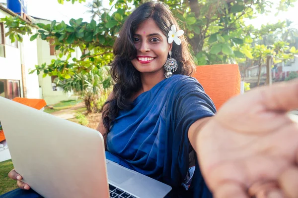 Азиатская фрилансерша, сидящая в кафе в синем стильном сари сари, работающая на ноутбуке и улыбающаяся фотографирующая портретная селфи. — стоковое фото