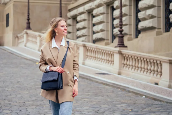 Outdoor portret van jonge mooie modieuze vrouw dragen trendy jas met kleine schoudertas, wandelen in de straat van europese Chezh Praha stad — Stockfoto