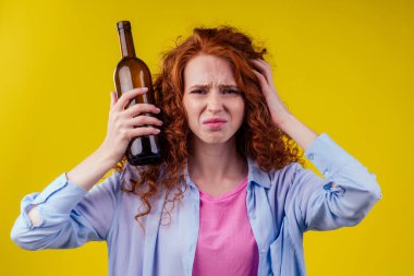 Kıvırcık kızıl saçlı kadın bira içiyor ve csudio sarı arka planda kendini kötü hissediyor.