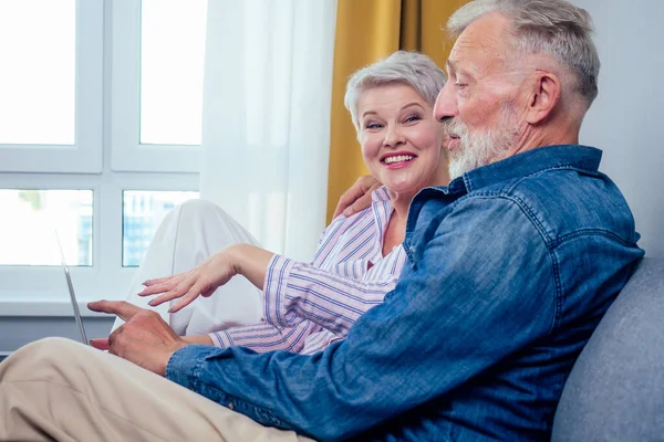 Pareja de ancianos en el amor sentado sofá gris en la sala de estar mirar a la pantalla portátil — Foto de Stock