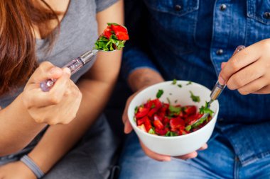 Genç Hintli çift oturma odasında oturmuş sebze salatası yiyorlar.