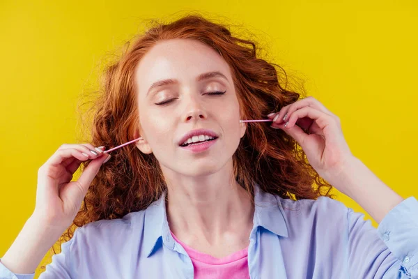 Rizado pelirroja caucásica mujer uso orejas palos en estudio amarillo fondo — Foto de Stock