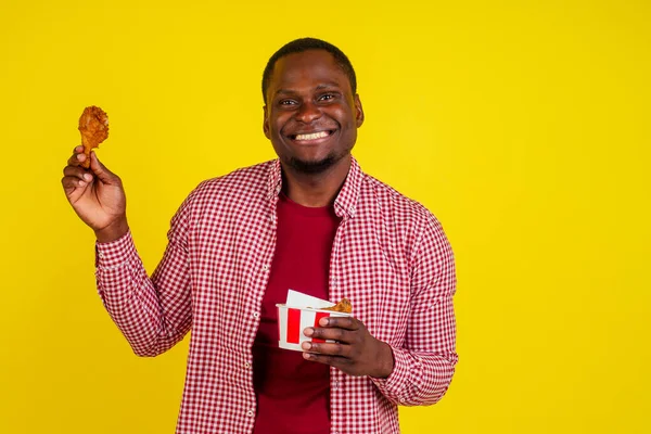 Смешной африканский американец ест жареную куриную ножку на жёлтом фоне студии — стоковое фото