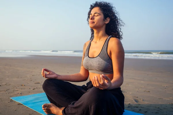 Afro america woman with curly hair and closed eyes deep breathing and calming herself on empty morning beach after surya namaskar — Stock Photo, Image