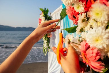 Okyanus kıyısındaki düğün kemeri için çiçek kompozisyonuyla çalışan bir dekoratör.