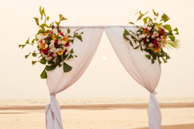 Açık havada güzel bir yaz düğünü. Düğün kemeri, gün batımında açık renk kumaştan, beyaz ve pembe çiçeklerden yapılmıştır.