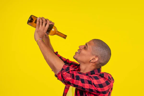 Latino brasileiro homem segurando garrafa de álcool em estúdio fundo amarelo — Fotografia de Stock