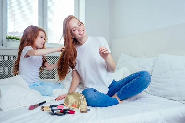 Güzel, seksi saçlı küçük kız makyaj yapıyor ve kızıl saçlı anneye saç stili yapıyor. Yatak odasındaki güzel, kızımsı spa gününde. — Stok fotoğraf