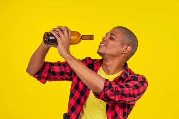 Latino brasileño hombre sosteniendo botella de alcohol en estudio amarillo fondo —  Fotos de Stock