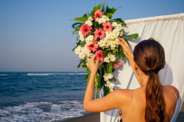 Okyanus kıyısındaki düğün kemeri için çiçek kompozisyonuyla çalışan bir dekoratör.