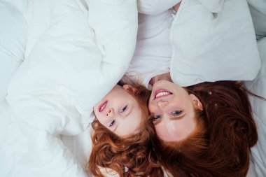 İki mutlu kızıl saçlı kız beyaz battaniyenin altında saklambaç oynuyorlar.
