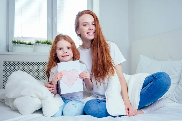 Şirin, seksi saçlı küçük kız, çizimi kâğıda döküyor, kızıl saçlı anneye yatak odasında veriyor. — Stok fotoğraf