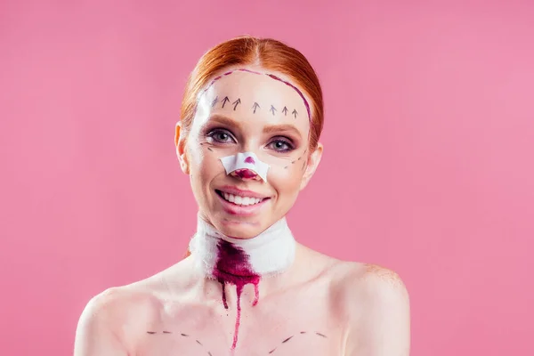 Ιατρική ασφάλιση. χαρούμενη κοκκινομάλλα κοκκινομάλλα γυναίκα με γραμμές στο πρόσωπό της και αίμα επίδεσμου στο λαιμό σε στούντιο ροζ φόντο — Φωτογραφία Αρχείου