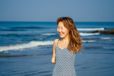 Mutlu Asyalı kolsuz kadın tropik sahilde gülümsüyor.