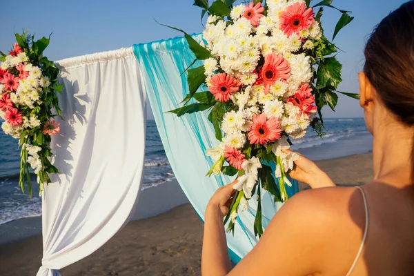 Decorador trabalhando com composição de flores para arco de casamento na praia do oceano — Fotografia de Stock