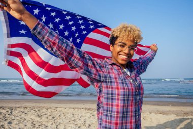 Güneşli tropik plajda bayrak tutan mutlu Afro-Amerikan kadını. 4 Temmuz Bağımsızlık Günü konsepti.