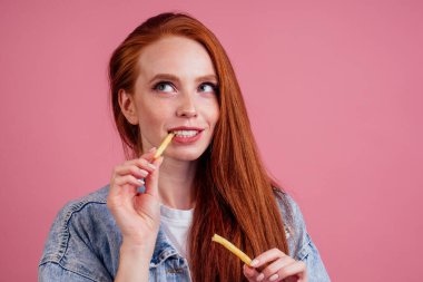 Şirin, uzun, seksi, kızıl saçlı kadın pembe stüdyoda patates kızartması ve karton kutu tutuyor.