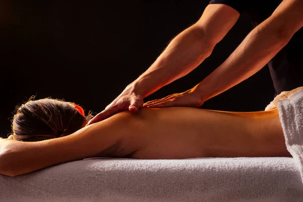 Mujer india joven acostada en la mesa y recibiendo masaje ayurvédico con aceite orgánico o meleyed en cuarto oscuro. Masajista macho vertiendo hacia atrás cliente — Foto de Stock