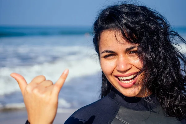 Индийская женщина с белоснежной улыбкой девушка в гидрокостюме показывает жест махало шака знак рукой сигнал, говорящий привет на райском пляже — стоковое фото