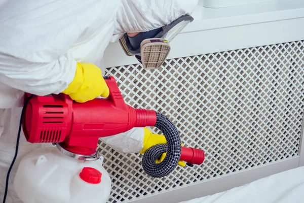 Haşere kontrol görevlisi yerde yatıyor ve yatak odasına böcek ilacı sıkıyor.