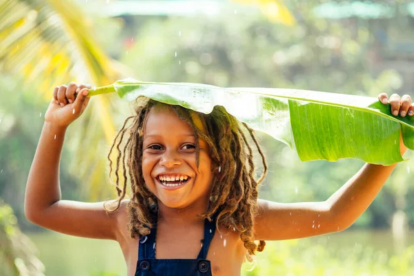 Маугли индийский мальчик с дредами волосы скрываются держа банановый лист в качестве крышки дождя в тропических зеленых лесов фоне — стоковое фото