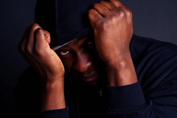 Тривожний молодий афроамериканський американець у сірому капелюсі та чорному халаті з капюшоном, що ховається від студії зловмисника s blow attack — стокове фото