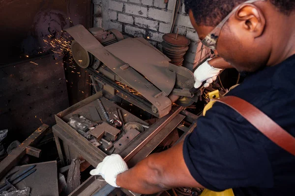 Martillo industria pequeña empresa concept.african hombre americano vestido con ropa histórica está martillando en el yunque. Un herrero forja un producto metálico — Foto de Stock