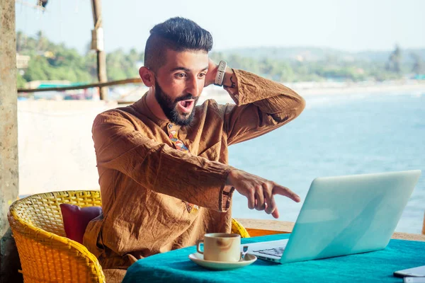 Atractivo trabajador egipcio masculino está utilizando la computadora en la cafetería con fondo de mar — Foto de Stock