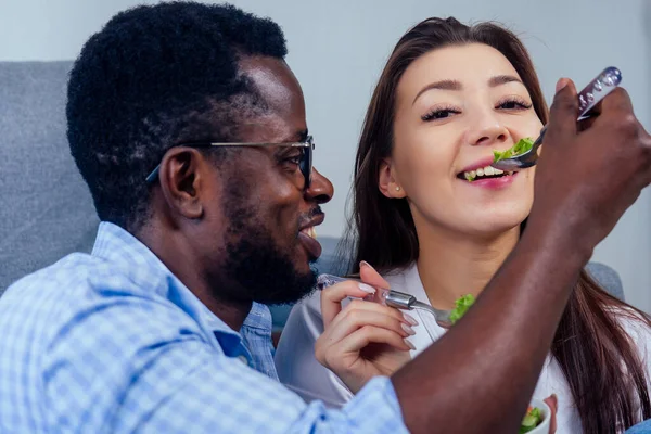 african american man eating salad with woman in living room