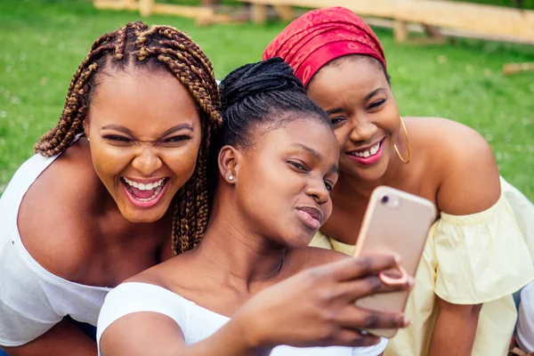 Portrait of three beautiful african-american women afro braids dreadlocks and turban taking pictures of yourself on the phone in the park at a picnic,sisters on vacation — Stock Photo, Image