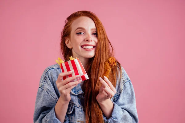 Ziemlich lange rothaarige Ingwermädchen essen Pommes Huhn im Studio rosa Hintergrund — Stockfoto