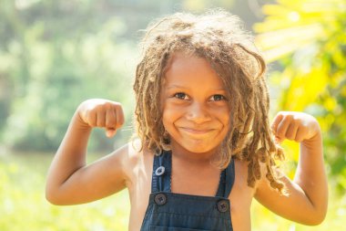 Mowgli indian boy with dreadlocks hair showing muscle arms in tropics green forest background clipart
