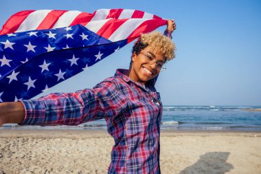 Güneşli tropik plajda bayrak tutan mutlu Afro-Amerikan kadını. 4 Temmuz Bağımsızlık Günü konsepti.