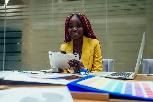 Kvinna modedesigner med afro flätor dreadlocks arbetar på hennes ateljé eller tryckeri. kosmetisk distributör arbetar på kontoret — Stockfoto