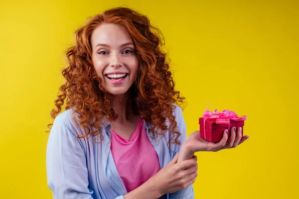 Rödhårig lockigt ingefära kvinna som håller presentförpackning i studio gul bakgrund. mödrar dag och åttonde marsor St. Alla hjärtans dag koncept — Stockfoto