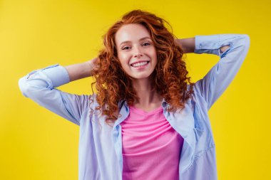 Mutlu, kızıl saçlı, kıvırcık saçlı, güzel yüzlü, stüdyo sarı arka planda pamuk pembe gömlekli bir kadın.
