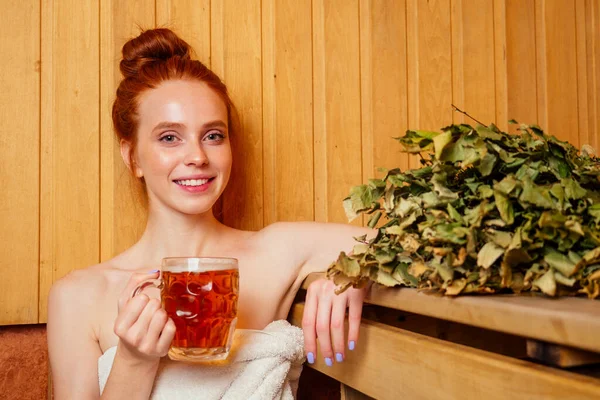 Pelirroja pelirroja mujer humeante en la casa de baños con escoba grupo ruso bebiendo beers.she disfrutar de la sauna finlandés spa — Foto de Stock
