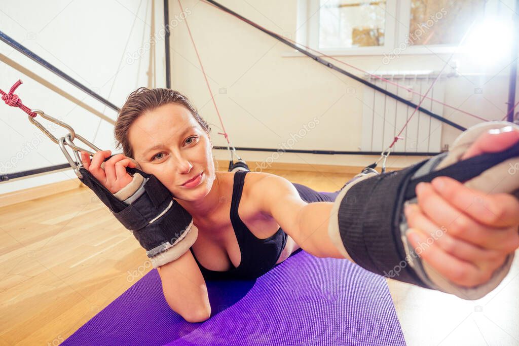 Sporty young caucasian woman doing stretching exercises of full body muscles workout on stretch aerobic aero strap in gym,yogi mat