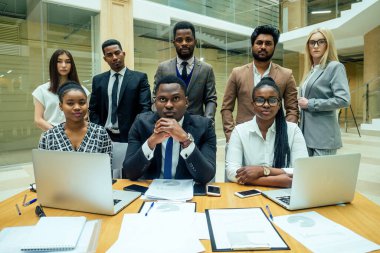 Ofiste çalışan bir grup başarılı Afro-Amerikalı, Avrupalı, Arap ve Koreli işadamı ve iş kadını büyük cam pencereli