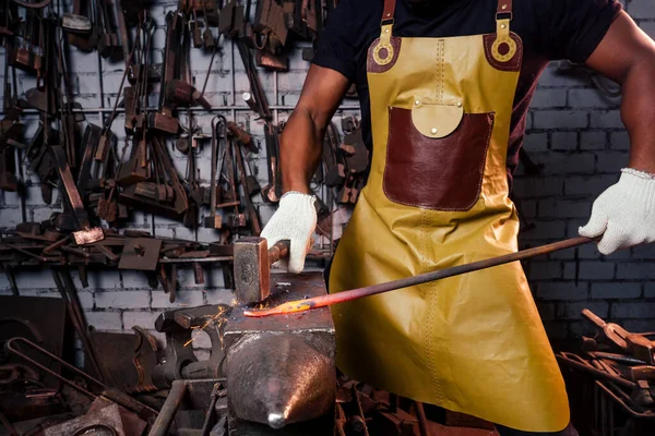 Knappe Afrikaanse amerikaanse smid mannelijke werknemer werken in de werkplaats, het dragen van lederen schort — Stockfoto