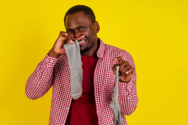 Недовольный африканский американец закрывает нос, чувствует неприятный запах носков, носит повседневную красную футболку на студийном жёлтом фоне — стоковое фото