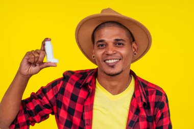 Latin Brezilyalı adam stüdyo sarı arka planda astım spreyi kullanıyor.